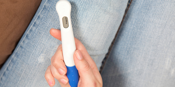 Woman holding a pregnancy test wondering "can you get pregnant on your period?"