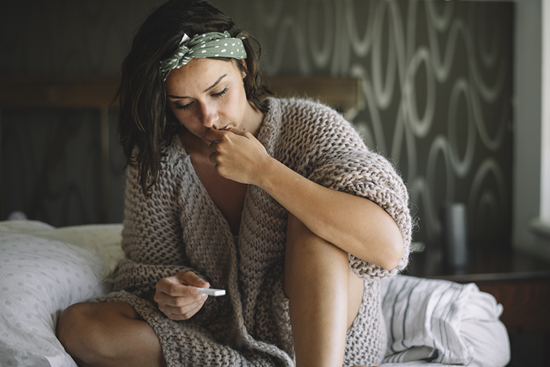 woman sitting on a bed looking at a pregnancy test